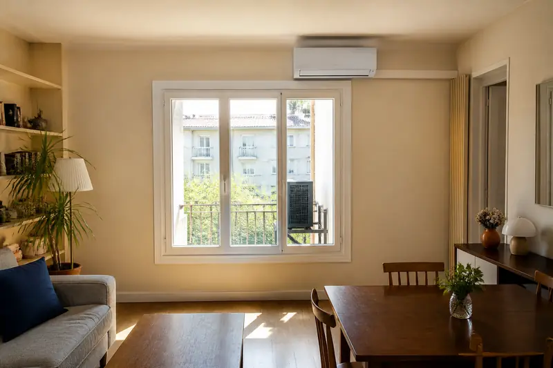 Climatiseur mural blanc installé au-dessus d'une fenêtre dans un salon lumineux